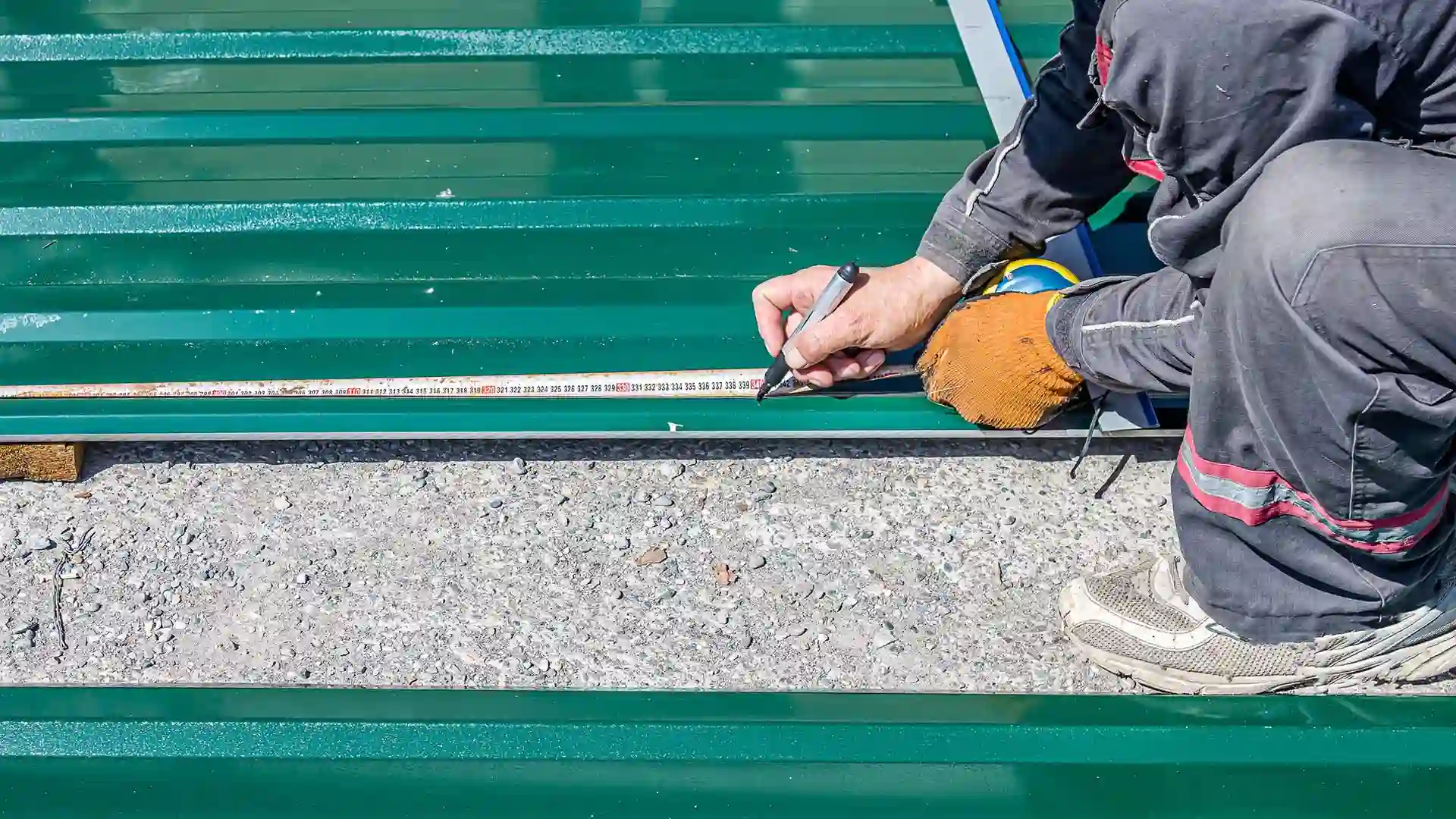 Couvreur mesurant un panneau de bac acier vert pour estimer le prix de pose au m2 d'une toiture.