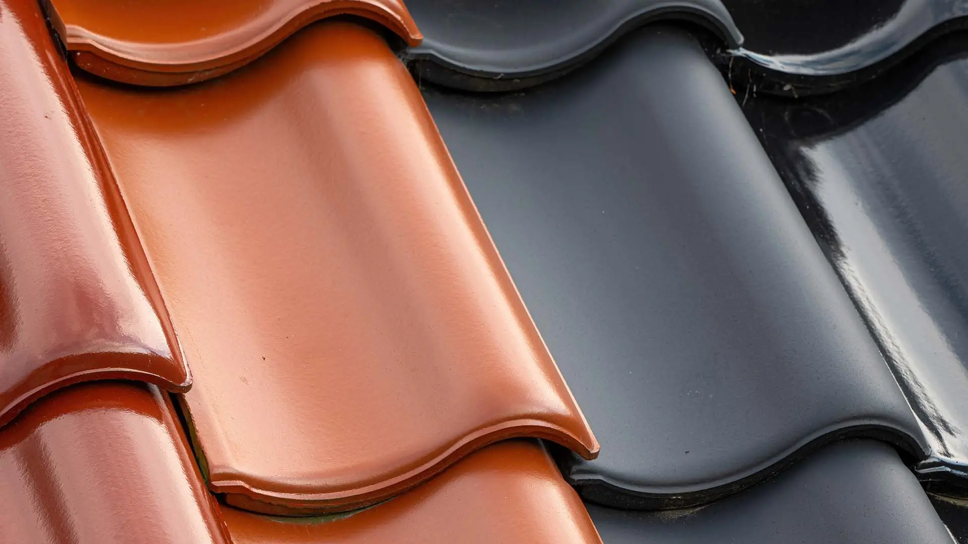 Gros plan de tuiles de toiture mécaniques en terre cuite de couleurs rouge et noire pour un comparatif de prix et de modèles.