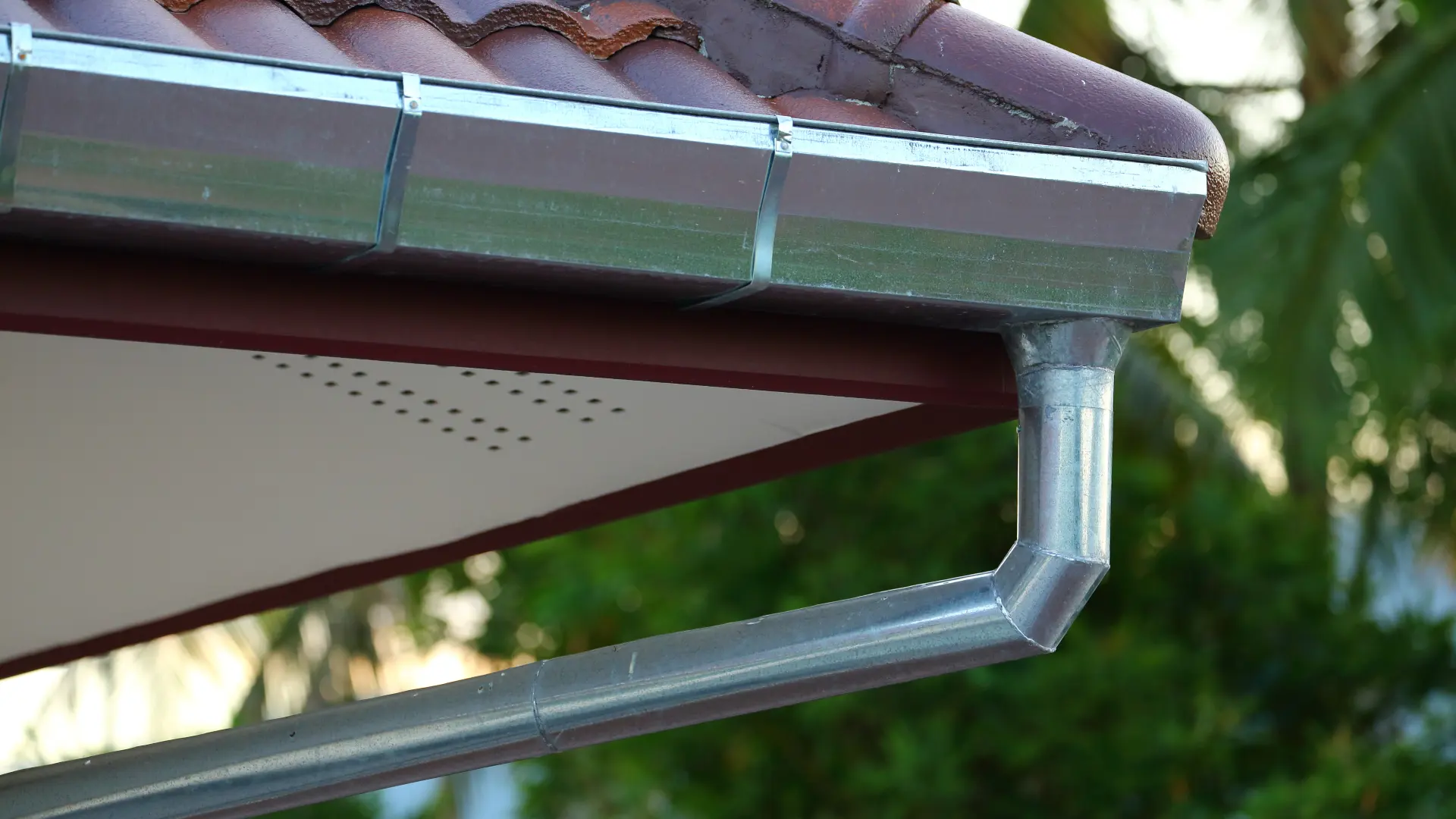 Gouttière en acier galvanisé neuve installée sous un toit de tuiles, avec naissance de descente d'eaux pluviales. Utile pour estimer le prix de vos travaux.